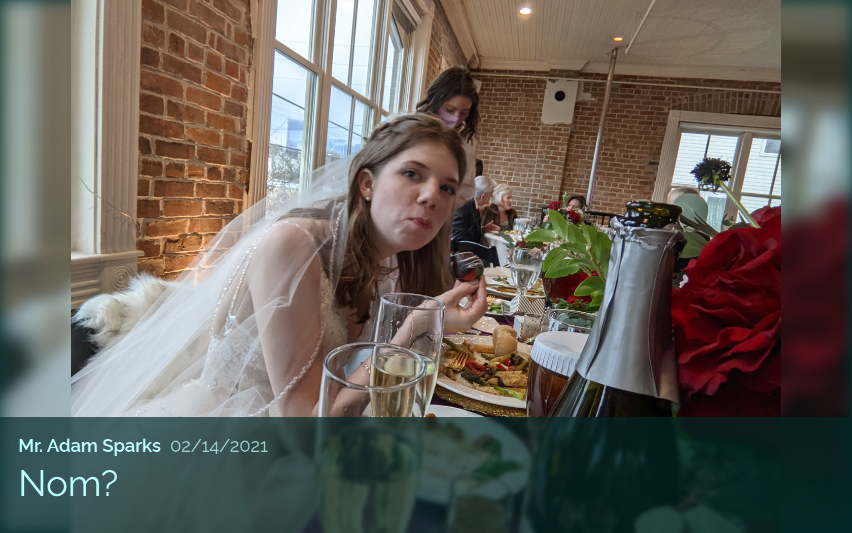 Bride in a wedding dress eating at a table during a reception, looking playfully at the camera. Caption reads “Nom?” with the name Mr. Adam Sparks and date 02/14/2021.