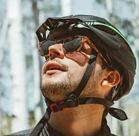Man in a helmet and sunglasses gazing thoughtfully upward in a city setting, looking toward the logo in the center as if ready for an adventure.